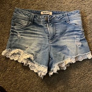 Blue denim slightly purposely ripped shorts with white lace trim. Size 3.